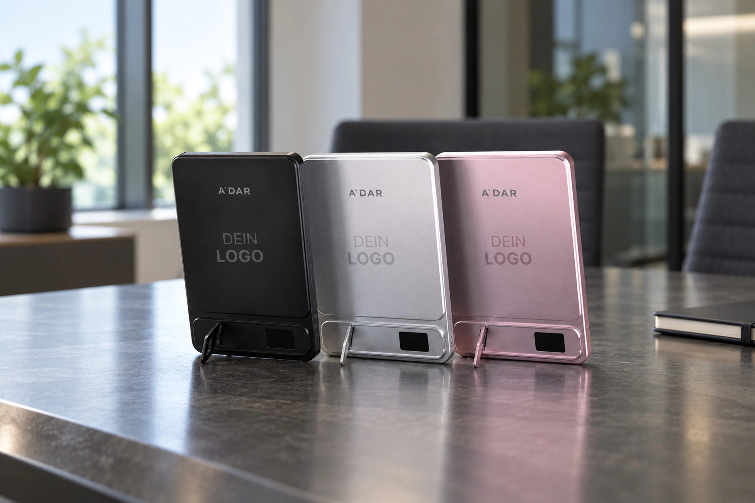 Drei AdarCharge Powerbanks in Schwarz, Silber und Pink auf einem Bürotisch